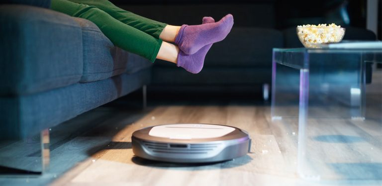 Robot vacuum patrols living room while someone sits on couch