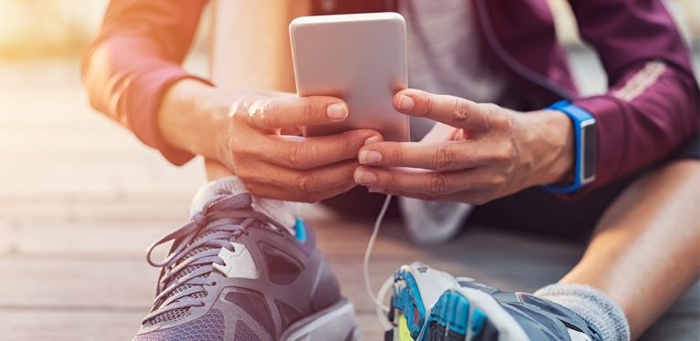 Person sitting on ground wearing running shoes and looking at phone
