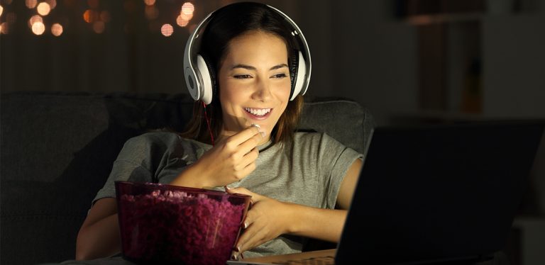 Woman eating popcorn, wearing headphones, and watching something on her laptop