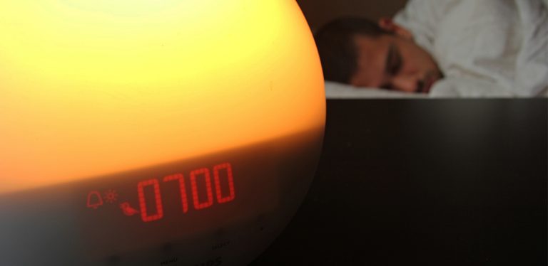 Light alarm clock with man sleeping in bed in background