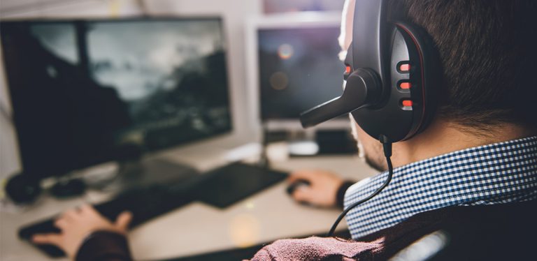 Man wearing a headset playing game on dual monitors