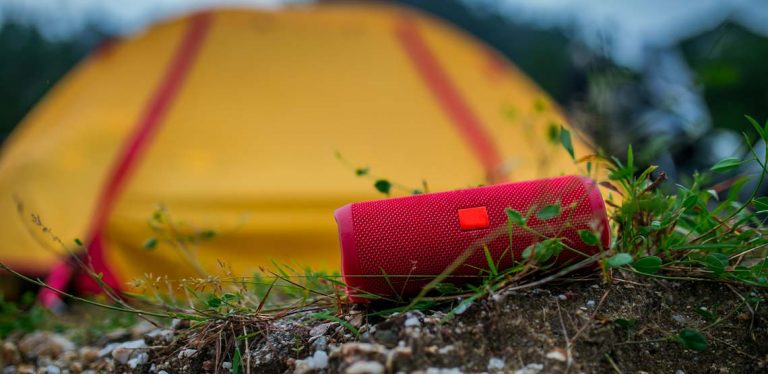A red outdoor speaker sitting in the grass in front of a yellow tent.