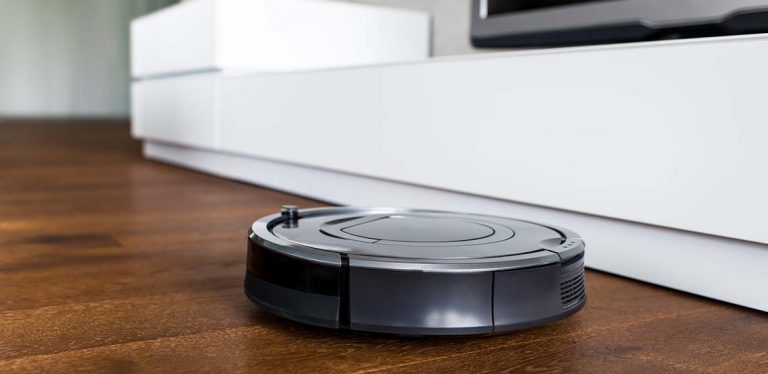 A black Roomba driving around on brown wooden floors.